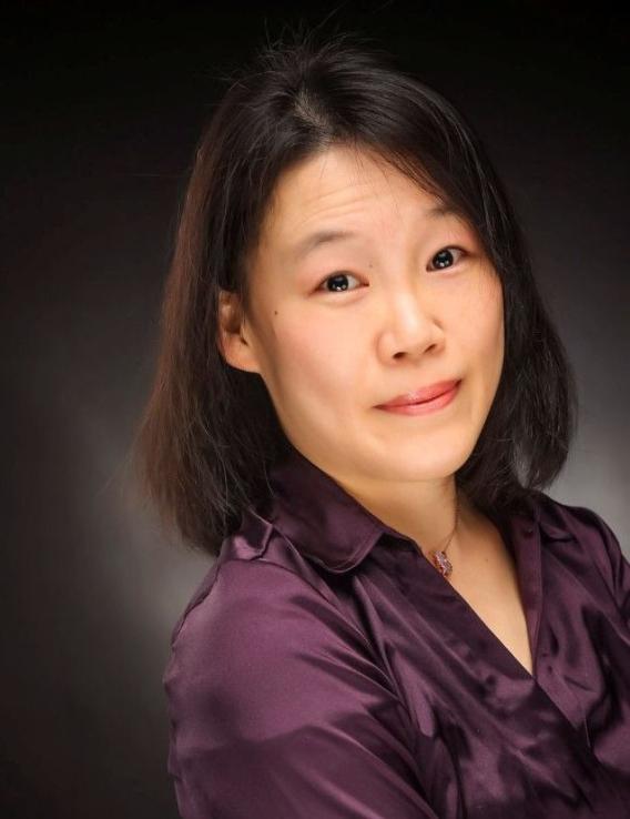 Photograph: Woman with dark hair, purple shirt, subtle smile.