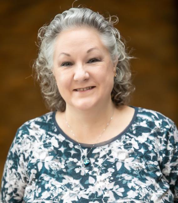 Smiling woman with grey curly hair in a patterned shirt.