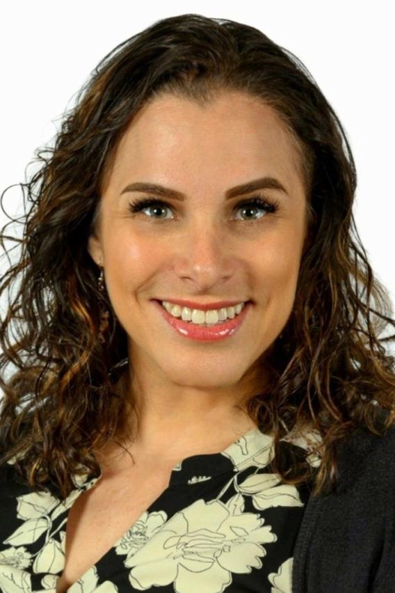 Smiling woman with dark, wavy hair and a black floral top.