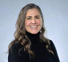 Smiling woman with long brown and gray hair, wearing a black turtleneck.