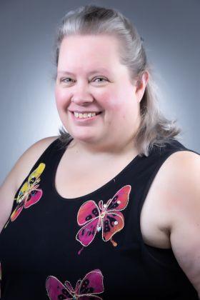 Smiling woman with graying hair in a black top with colorful butterflies.