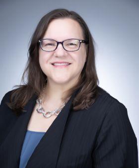 Smiling woman in glasses and a dark professional jacket.
