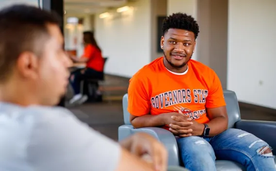 A young man in an orange GovState tshirt sitting in the lounge area