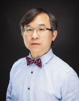 Headshot of an Asian man wearing glasses, a blue shirt, and a striped bow tie.