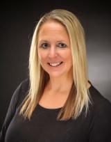 Smiling woman with long blonde hair and black shirt against a dark background.